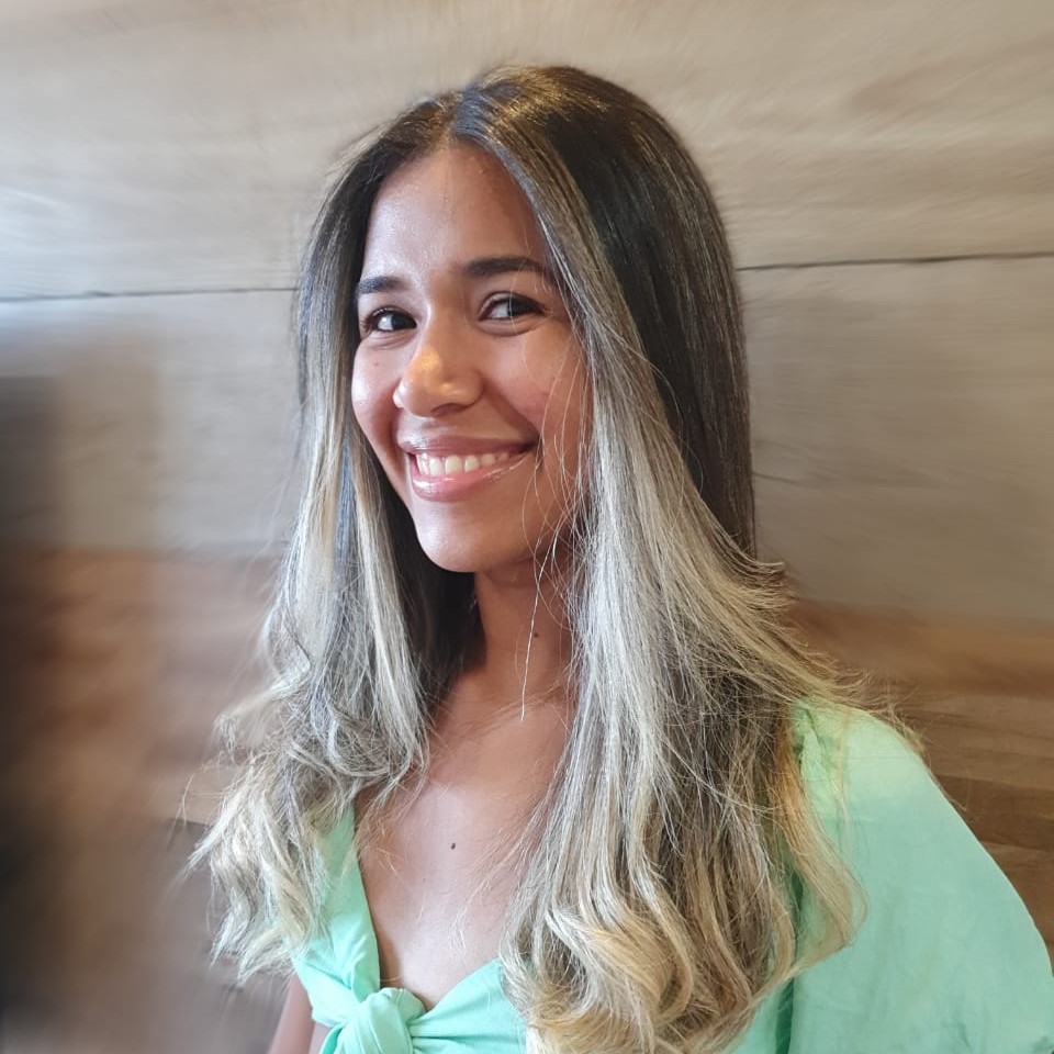 Foto da Maynara. Mulher parda de cabelo escuro com mechas loiras sorrindo